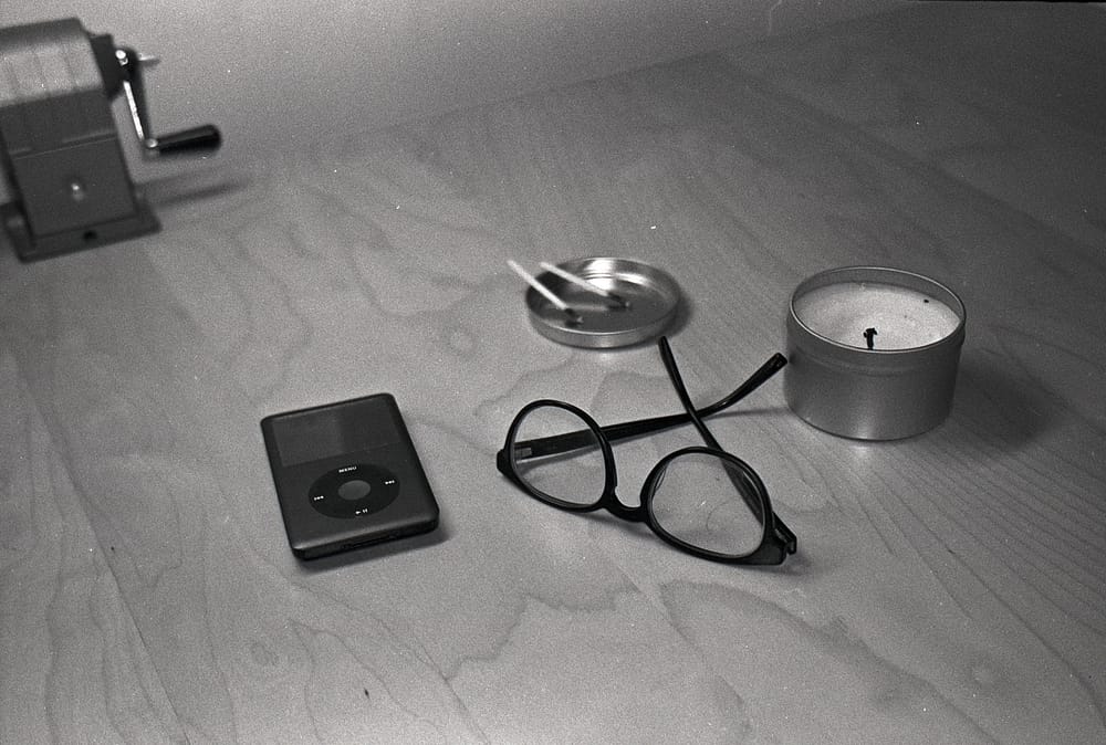 Black and white film photo of iPod, glasses, and candle on my desk.