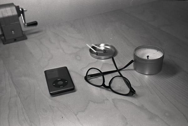 Black and white film photo of iPod, glasses, and candle on my desk.