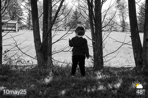 Black and white photo of boy standing by trees
