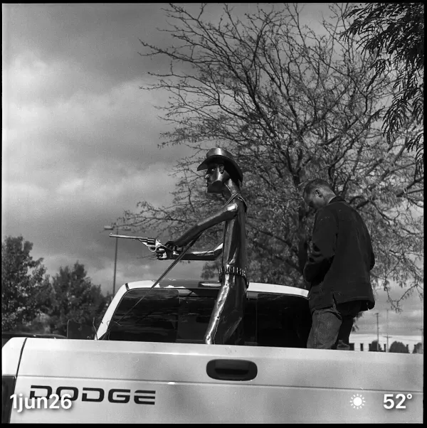 Black and white film photo of cowboy sculpture in back of Dodge pickup