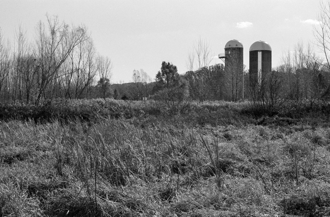 Black and white film photo of fields with 2 silos in distance