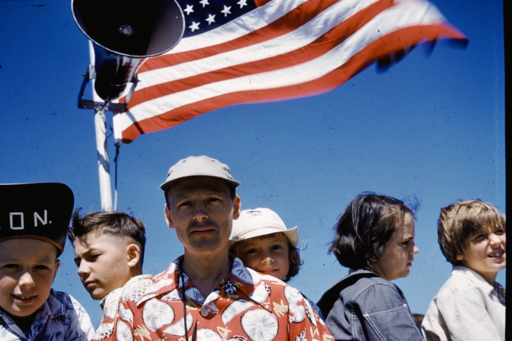 Photo of people standing under a flag and speaker (1950s)