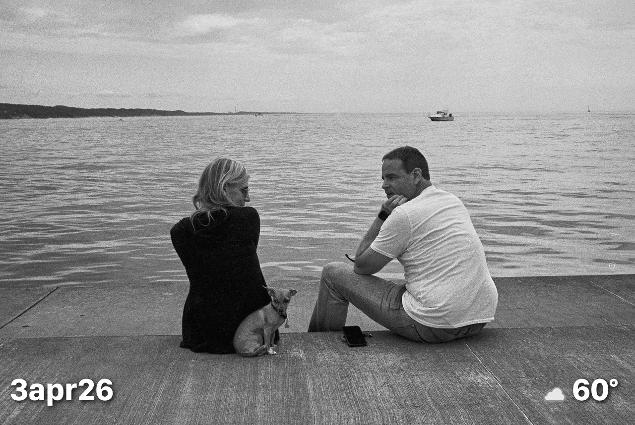 Black and white film photo of couple with small dog sitting on pier