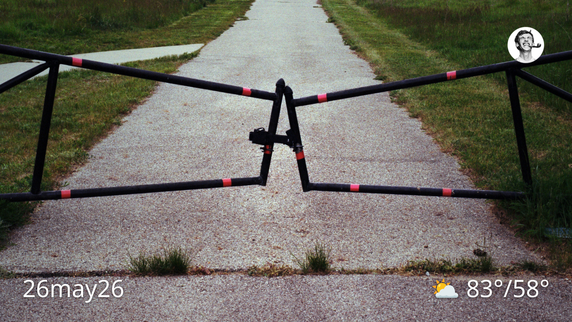 Color film photo of gate in front of paved path through a field