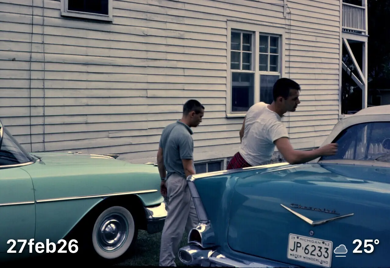 2 men walking behind back of a 1957 Chevy