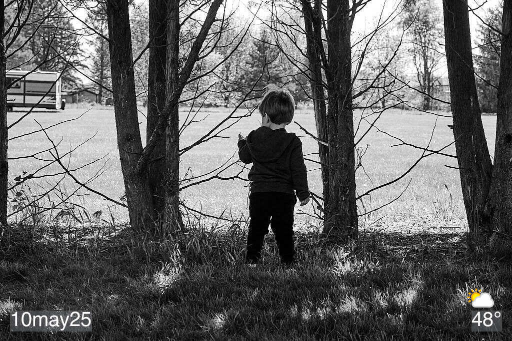 Black and white photo of boy standing by trees
